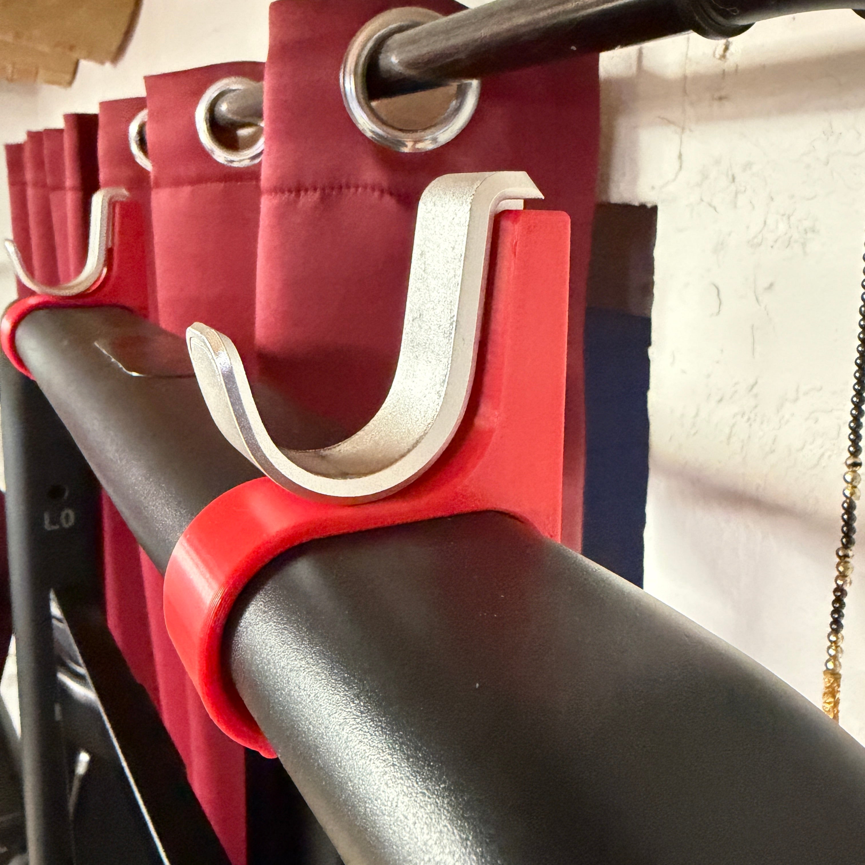 Close-up of a red U-shaped metal clip attached to a black bar with a blurred background.